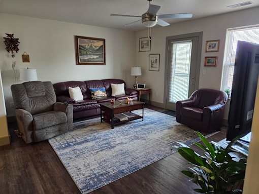 A living room with a brown leather couch, a grey armchair, a brown armchair, a coffee table, and a ceiling fan.